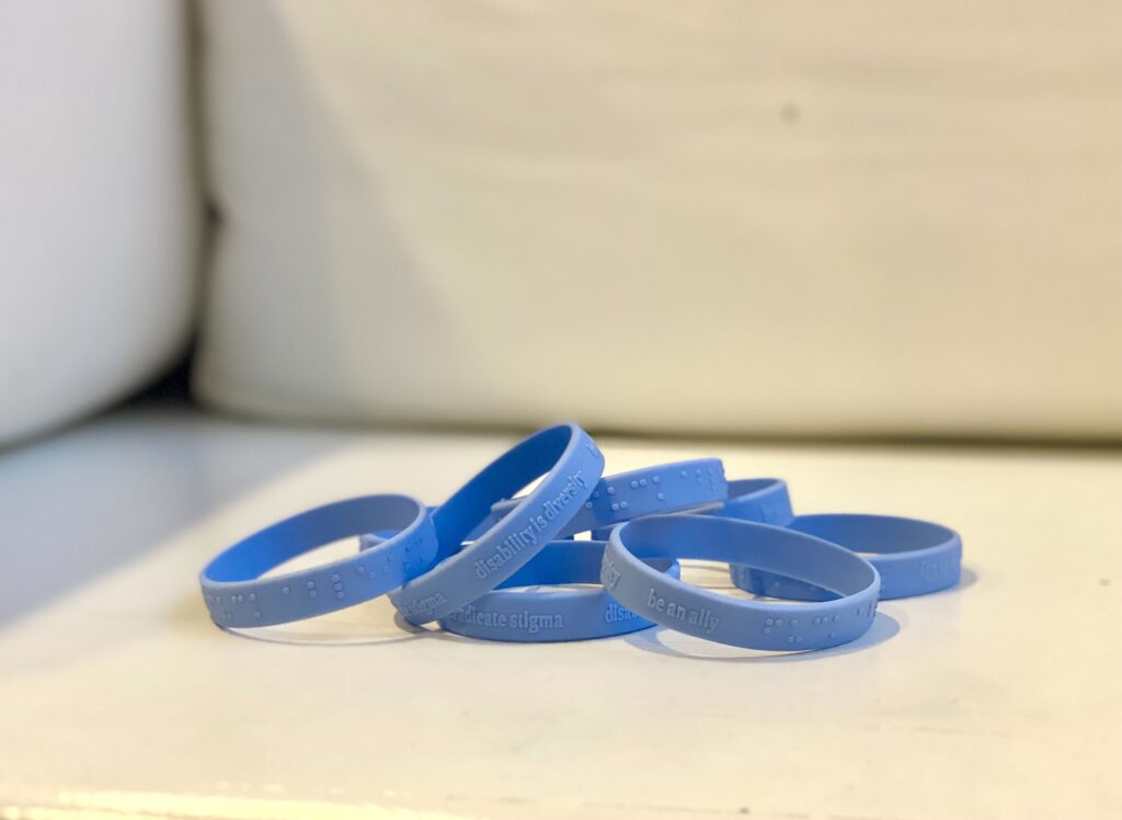 eight Blue disability allyship wristbands laying on a white surface