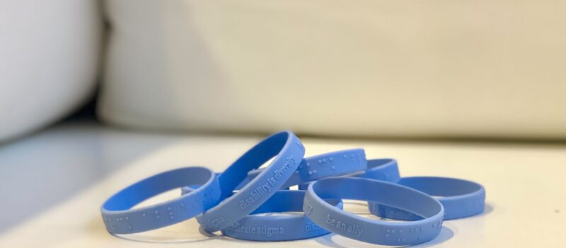 eight Blue disability allyship wristbands laying on a white surface