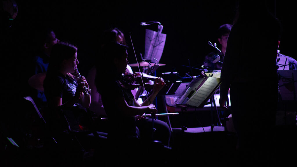 Orchestra playing under purple light.