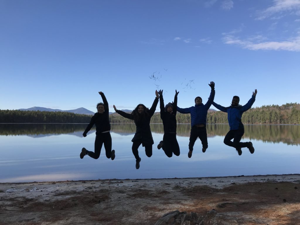 People jumping against backdrop of lake and trees. 